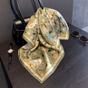 Close-up of a floral silk square scarf elegantly draped over a black leather handbag