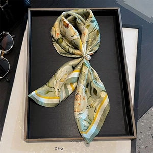Detailed macro view of green floral silk scarf featuring elegant white roses and a pearl buckle