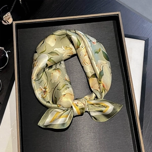 Detail of silk floral scarf showing green leaf lily prints and soft texture on black tray