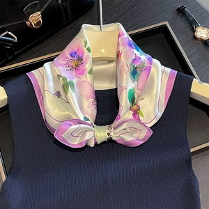 Close-up of silk floral square scarf tied on a navy knit top with elegant accessories
