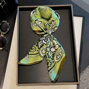 Detail eines grünen Seidentuchs mit Blumendruck und Perle auf einem schwarzen Tablett
