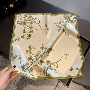 Detail eines Seiden-Halstuchs mit botanischem Blatt- und Schmetterlingsdruck auf beigem Stoff
