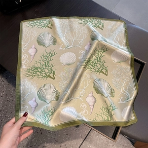 Detailed texture of square silk scarf with sea coral and shell print on gold fabric