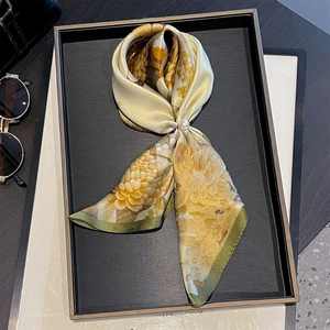 Floral print silk scarf in golden yellow with pearl buckle on a luxury black display
