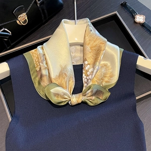 Detail of silk floral scarf tied in a bow on a navy knit vest with elegant accessories
