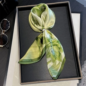 Détail d'un foulard en soie verte à fleurs avec une boucle en perles sur un plateau