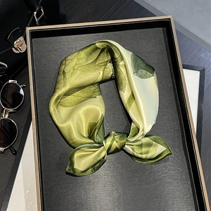 Élégant foulard en soie verte à motif floral sur un plateau avec lunettes de soleil