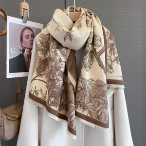 Vue détaillée du motif floral rétro et des pompons fins sur l'écharpe en faux cachemire