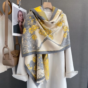 Détail d'une écharpe jacquard crème avec fleurs jaunes et franges sur un manteau