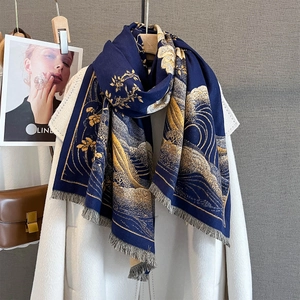 Détail d'une écharpe bleu marine à motifs de vagues dorées et franges sur manteau blanc