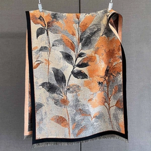 Détail d'une écharpe fleurie montrant des motifs de feuilles orange et des franges