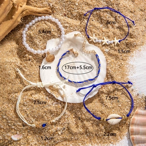 Detail of five bohemian summer bracelets with shells and evil eye on beach background