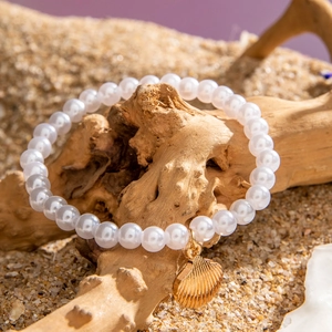 Close-up of beaded beach bracelet featuring a gold shell charm and imitation pearls on sand