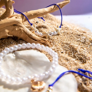 Close-up of beach bracelets with starfish, faux pearls and shell on sand background