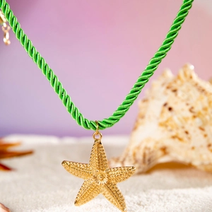 Collier bohème avec pendentif étoile de mer dorée sur cordon vert dans le sable blanc
