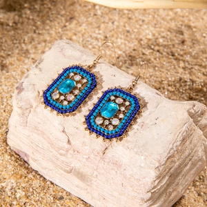 Detailed shot of bohemian tassel earrings with blue stones on natural beach rocks