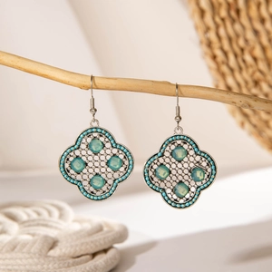 Close-up of bohemian hollow clover earrings with teal beads on a natural wooden branch