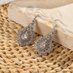 Macro detail of silver bohemian earrings with waterdrop crystals on marble background