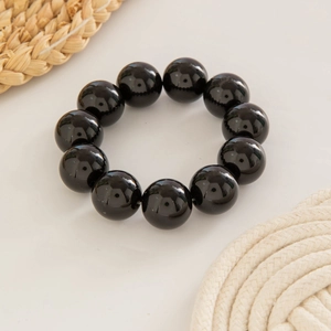 Close-up of glossy black obsidian beaded bracelet on a natural straw mat backdrop