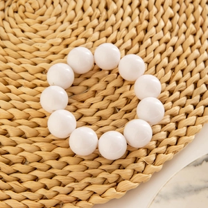 Close-up of polished white resin beaded bracelet on a woven mat with marble detail