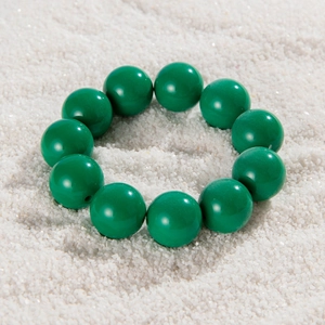 Detailed macro view of large polished green beads on a minimalist white sand background