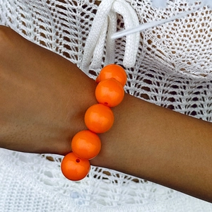Close-up of bright orange large beaded bracelet on wrist with crochet background