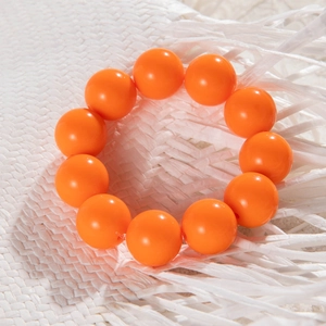 Detail of chunky orange resin beads bracelet on white textured background in 45-degree view