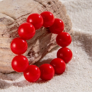 Detailed view of large vibrant red round beaded bracelet on a neutral stone background