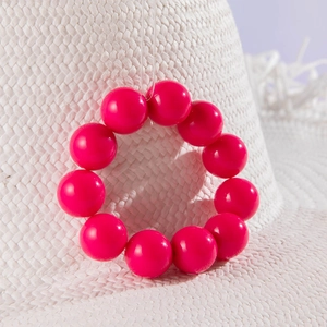 Close-up of bright pink glossy beads on an ethnic bracelet against a straw hat background
