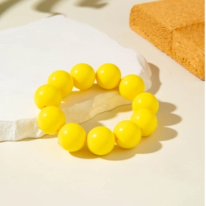 Macro shot of vibrant yellow round beads bracelet on white stone textured background