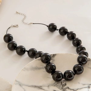 Detail of bohemian necklace featuring large glossy black beads and silver lobster clasp