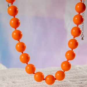 Macro detail of vibrant orange resin beads on a bohemian necklace with silver extender chain
