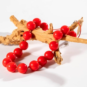 Detail of large red beaded necklace displayed on a textured brown wooden branch