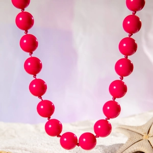 Close-up of bright pink beaded bohemian necklace with handmade knots on beach sand
