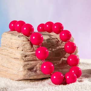Detail of bright pink chunky beads necklace on light textured stone with sand