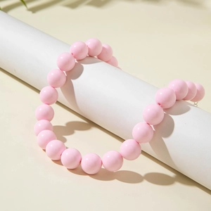 Detail of pink beaded necklace displayed on a white cylindrical stand with leaf shadows
