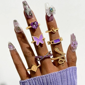 Ensemble de 7 bagues dorées avec papillon et pierres violettes sur une main