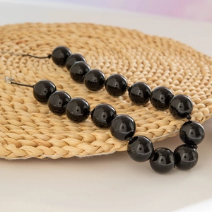 Bohemian chunky black bead necklace with glossy finish on a natural woven mat background