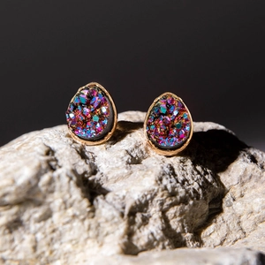 Dettaglio macro di orecchini a goccia in oro rosa con pietre druzy arcobaleno
