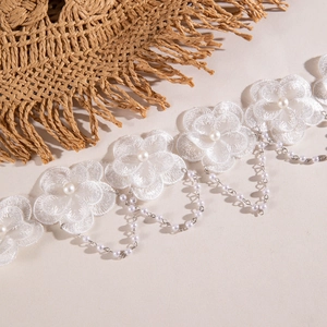 Détail d'un ras de cou en dentelle blanche avec broderie florale, perle et chaîne argentée
