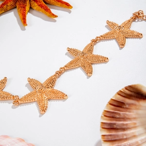 Golden starfish chain accessory with textured metallic finish on white beach background