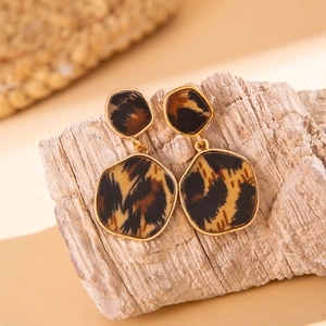 Macro view of geometric gold alloy earrings with leopard print inserts on wood