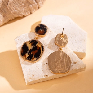 Detail of leopard print geometric earrings on textured stone with warm lighting