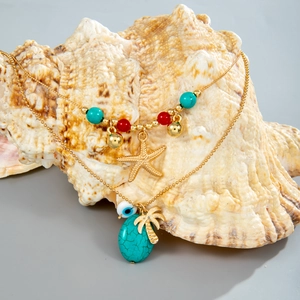 Detail einer mehrlagigen Goldkette mit Seestern, Palmenanhänger und Türkisperlen