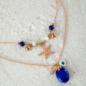 Detail einer böhmischen Goldkette mit Seestern, Palme und Bösem Blick auf weißem Sand
