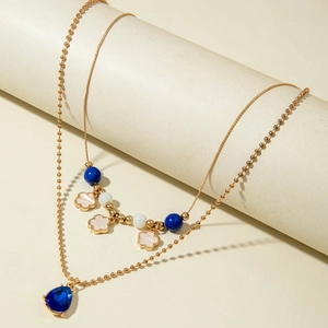 Detail einer mehrlagigen Goldkette mit blauem Edelstein und weißen Blütenanhängern