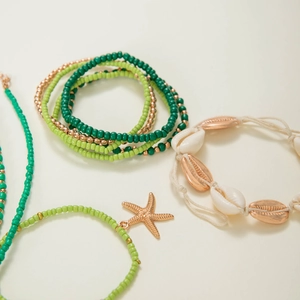 Detail of bohemian shell and starfish beaded bracelets in green, gold, and white tones