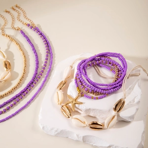 Detail of seashell beads and gold starfish pendant on a purple bohemian jewelry set