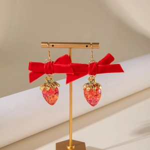 Détail de boucles d'oreilles fraise avec nœuds en velours rouge sur support doré