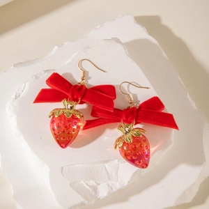 Détail de boucles d'oreilles fraises avec nœuds en velours et feuilles dorées sur socle